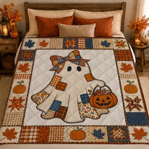 May include: A quilted throw blanket featuring a central ghost character wearing a plaid bow and carrying a jack-o'-lantern bucket. The quilt is bordered by a patchwork pattern of autumn leaves, pumpkins, and plaid squares in orange, blue, and white.