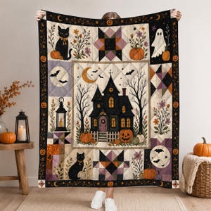 May include: A quilted throw blanket featuring a central haunted house illustration surrounded by black cats, ghosts, pumpkins, bats, and floral motifs. The design includes geometric star patterns, a crescent moon, and a dark border with orange pumpkins.