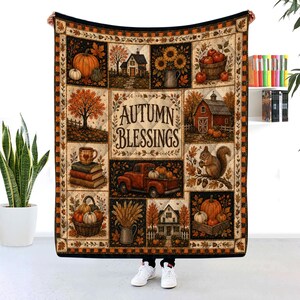 May include: A rectangular throw blanket featuring a patchwork design with autumn-themed illustrations including pumpkins, a red truck, a barn, a squirrel, and houses. The center panel displays the text AUTUMN BLESSINGS in a dark brown font.