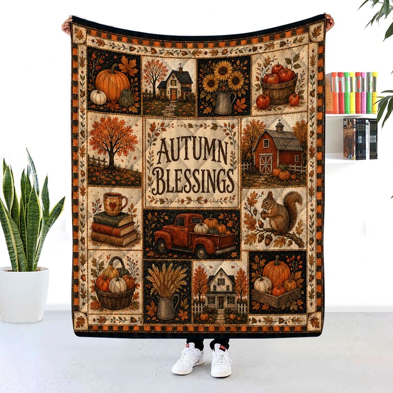 May include: A rectangular throw blanket featuring a patchwork design with autumn-themed illustrations including pumpkins, a red truck, a barn, a squirrel, and houses. The center panel displays the text AUTUMN BLESSINGS in a dark brown font.