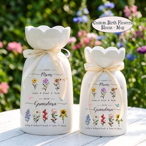 May include: Two white ceramic vases with a floral design and the text "First Mom - Now Grandma." Each vase has a cream-colored ribbon tied around the neck. The vases are decorated with colorful flowers and butterflies. The text "Custom Birth Flowers Bloom - Mug" is also visible.