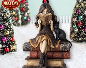 May include: A hanging ornament featuring a figure with long brown hair wearing a brown dress, sitting on a stack of four vintage-style books while reading an open book. A small black cat sits beside the figure on the top book.