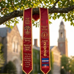 May include: Maroon graduation sash with gold trim, hanging from a tree branch. The sash displays the text "Fruit of the Roots", "Charmaine Burrell", "Master of Social Work", and "Class of 2026". The Bridgewater State University logo is also visible.