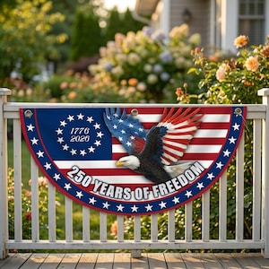 May include: A patriotic banner with a design featuring the American flag, an eagle, and the text "250 YEARS OF FREEDOM." The banner is red, white, and blue, with stars and stripes. The banner is hanging on a white fence.