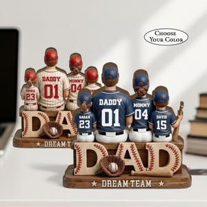 May include: Baseball-themed family figurines. The figurines are wearing baseball jerseys with the words "Daddy" and "Mommy" and numbers. The base of the figurines reads "DAD" and "DREAM TEAM". The text "CHOOSE YOUR COLOR" is also visible.