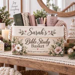 May include: A rectangular fabric storage basket with rope handles, featuring floral illustrations and the text Sarah's Bible Study Basket and Made for quiet mornings with God. The basket contains a Holy Bible, notebooks, pens, and a pink tumbler.