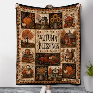 May include: A quilted throw blanket featuring a patchwork design with autumn-themed illustrations including pumpkins, sunflowers, a red barn, a squirrel, and a red truck. The center panel displays the text Autumn Blessings in dark brown lettering.