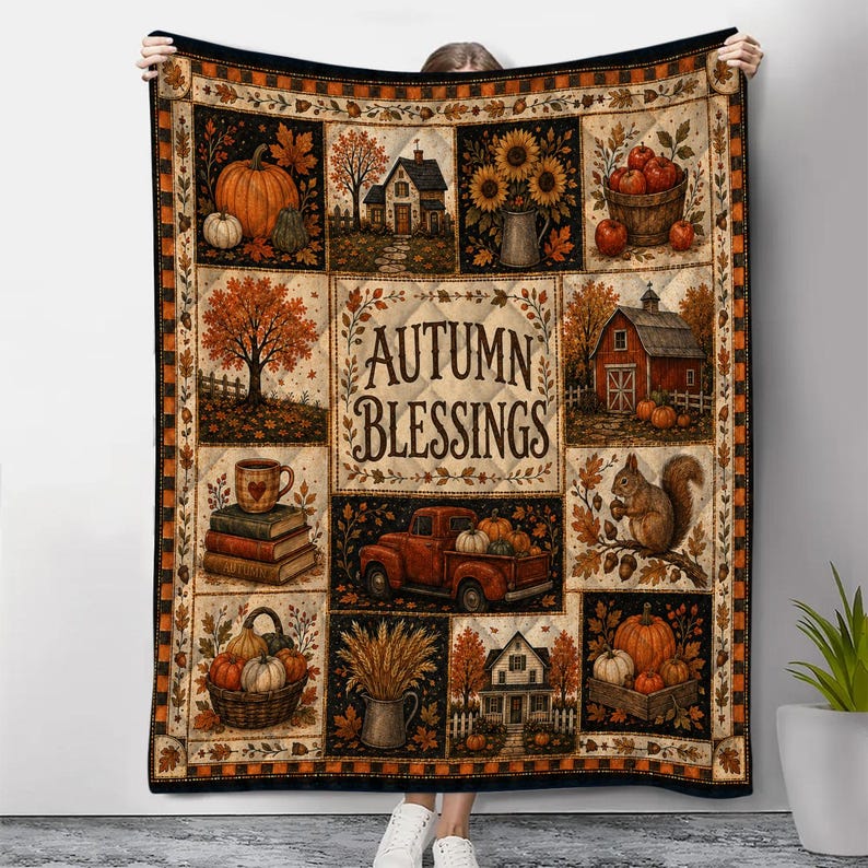 May include: A quilted throw blanket featuring a patchwork design with autumn-themed illustrations including pumpkins, sunflowers, a red barn, a squirrel, and a red truck. The center panel displays the text Autumn Blessings in dark brown lettering.