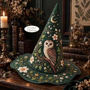 May include: A dark green quilted pointed hat featuring an embroidered brown owl perched on a branch, surrounded by white flowers, green leaves, and gold stars. A crescent moon is near the top. The text 4 Color Options is visible.