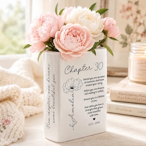 May include: A white rectangular ceramic vase filled with pink and white peonies. The front features the text Chapter 30, a floral illustration, the name Amelia, a poem, and EST. 1996. The side displays the text New chapter, new dreams, same beautiful you.