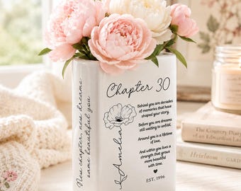 May include: A white rectangular ceramic vase filled with pink and white peonies. The front features the text Chapter 30, a floral illustration, the name Amelia, a poem, and EST. 1996. The side displays the text New chapter, new dreams, same beautiful you.