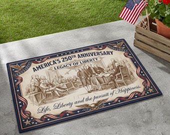 Op de afbeelding: Rechthoekige deurmat met een patriottisch ontwerp. De mat toont de tekst "AMERICA'S 250TH ANNIVERSARY LEGACY OF LIBERTY" en "Life, Liberty and the pursuit of Happiness." Het heeft een marineblauwe rand met rode en witte accenten. De afbeelding toont een historische scène.