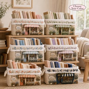 May include: Six rectangular fabric storage bins with rope handles, each printed with a bookshop storefront illustration labeled Emma's Bookshop, filled with various hardcover books, featuring floral borders and striped awnings in different colors.