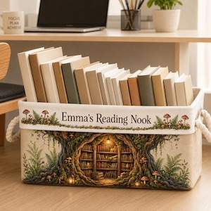 May include: A rectangular fabric storage bin with white rope handles, featuring a printed design of a tree trunk with a hollow library interior, mushrooms, and ferns. The text "Emma's Reading Nook" is printed on the front, filled with books.