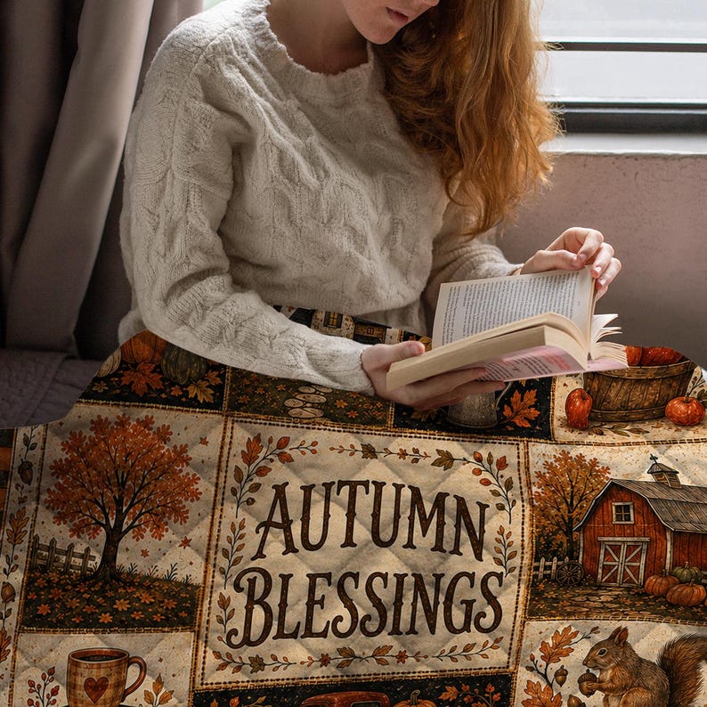 May include: A quilted throw blanket featuring a patchwork design with autumn-themed illustrations including trees, a red barn, pumpkins, and a squirrel. The central panel displays the text "AUTUMN BLESSINGS" surrounded by a decorative leaf border.