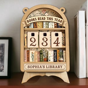 May include: Wooden bookshelf-shaped display with the text "BOOKS READ THIS YEAR" and the numbers "234". The display has a floral design and the text "SOPHIA'S LIBRARY". It is designed to track the number of books read.