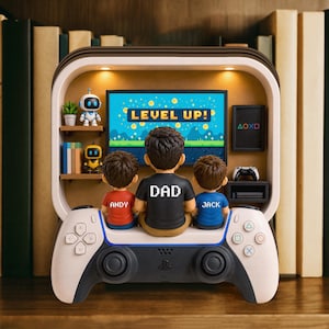 May include: A decorative gaming-themed figurine featuring a family of three, with the word "DAD" on the central figure's shirt. The figurine is set against a backdrop of a TV screen displaying "LEVEL UP!" and is mounted on a white and black game controller.