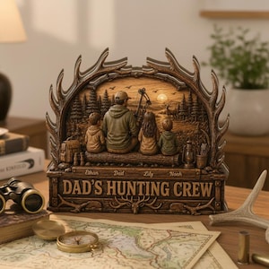 May include: A brown resin sculpture featuring a hunting scene with a father and three children. The sculpture is framed by antler-shaped elements and includes the text "Dad's Hunting Crew" and the names of the children. A bow and arrow are visible.