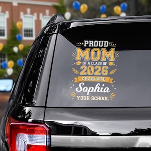 May include: A black car window sticker with the text "PROUD MOM of a class of 2026 Graduate Sophia YOUR SCHOOL" in yellow and white. The sticker has a graduation cap and laurel leaves design.