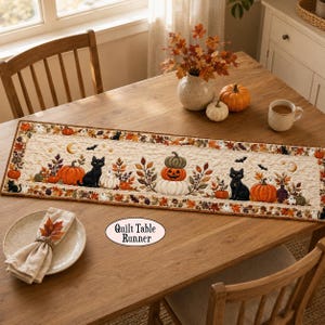 May include: A rectangular quilted table runner featuring a cream-colored background with a repeating pattern of black cats, orange pumpkins, autumn leaves, bats, and small ghosts. The border is decorated with fall foliage and tiny ghosts.