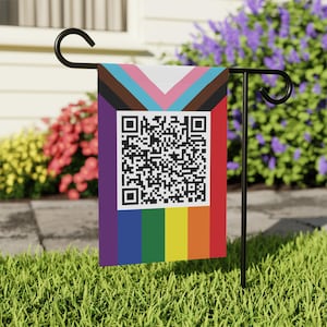 May include: A garden flag featuring a QR code and a design incorporating the colors of the Pride flag and the Progress Pride flag. The flag is rectangular and hangs from a black metal stand, displayed in a grassy yard.
