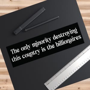 May include: A black rectangular sticker with white text that reads "The only minority destroying this country is the billionaires." A black pen and marker are above the sticker. A silver ruler is on the right.