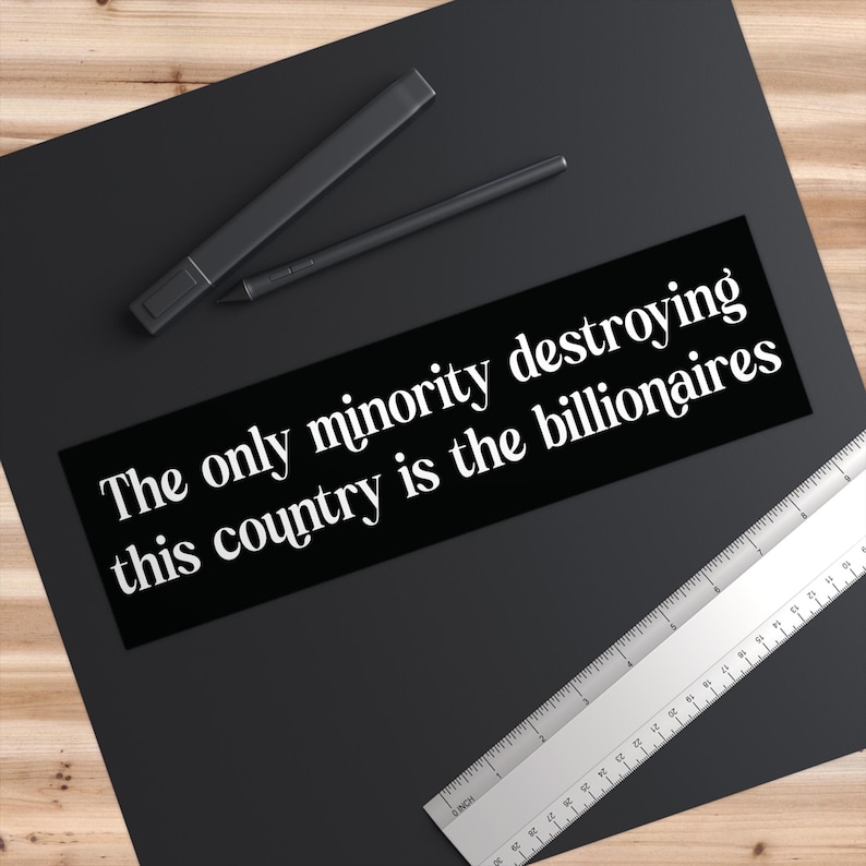 May include: A black rectangular sticker with white text that reads "The only minority destroying this country is the billionaires." A black pen and marker are above the sticker. A silver ruler is on the right.