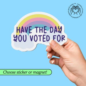 May include: A sticker or magnet with a rainbow design and the text "HAVE THE DAY YOU VOTED FOR." The sticker is held by a hand against a light blue background. A portion of each sale is donated to support good causes.