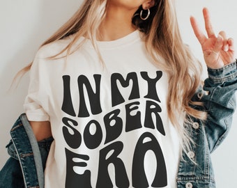 May include: White t-shirt with black text that reads "In My Sober Era" in a retro font.