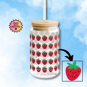May include: A clear glass tumbler with a bamboo lid and straw, adorned with a repeating pattern of red strawberries with green leaves. A small graphic shows a strawberry with the words "TRUMP SUCKS".