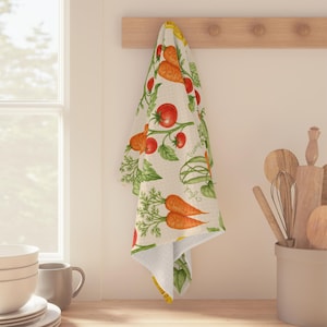 May include: A kitchen towel with a vegetable print, including carrots, tomatoes, and green leaves. The towel is hanging on a wooden rack. The design features the words "trump" and "luck" in script.