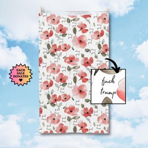 May include: White towel with a floral pattern of red watercolor flowers and green leaves. The words "fuck trump" are written repeatedly across the towel. A small image shows the words "fuck trump" with a watercolor flower.