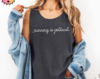 May include: Dark gray tank top with the white text "running is political". The sleeveless shirt is made of a soft material. A light blue denim jacket is draped over the shoulders.