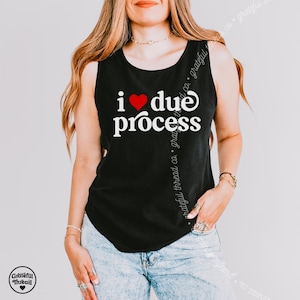 May include: Black tank top with the text "I ❤️ due process" in white, with a red heart replacing the word "love". The tank top is sleeveless and has a round neckline. The brand logo is in the bottom left corner.