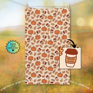 May include: A beige towel with a repeating pattern of orange pumpkins, coffee cups, bows, and leaves. A small inset shows a coffee cup with the text "TRUMP SUCKS". The towel is hanging on a clothesline.