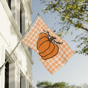 May include: A flag with an orange and white gingham pattern. The flag features a large orange pumpkin with a black outline. The words "fuck trump" are written on the flag.