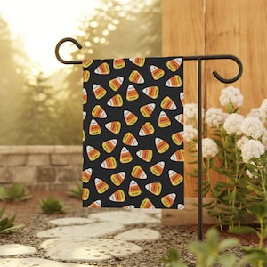 May include: A rectangular garden flag featuring a repeating pattern of candy corn shapes on a black background. Each candy corn is colored with white, orange, and yellow sections and includes the printed text "FUCK DONALD TRUMP" in black.