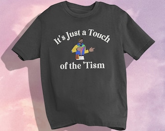 May include: A dark gray t-shirt with a white graphic print that says "It's Just a Touch of the 'Tism". The graphic also features a cartoon illustration of a person wearing a colorful outfit.