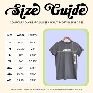 Pode incluir: Um guia de tamanhos para uma camiseta unissex de manga curta para adultos. O guia mostra as medidas para os tamanhos S a 4XL, com largura e comprimento em polegadas. A camisa &eacute; cinza e est&aacute; pendurada em um cabide de madeira.