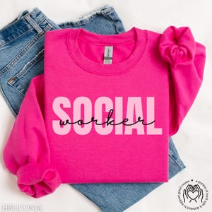 May include: Pink sweatshirt with the text "SOCIAL worker" in black and pink lettering.