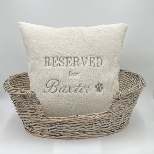May include: A white plush dog bed with a white pillow that says "RESERVED for Baxter" with a paw print.