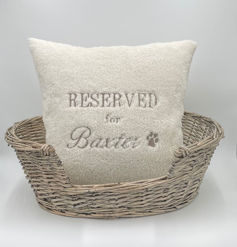 May include: A white plush dog bed with a white pillow that says "RESERVED for Baxter" with a paw print.