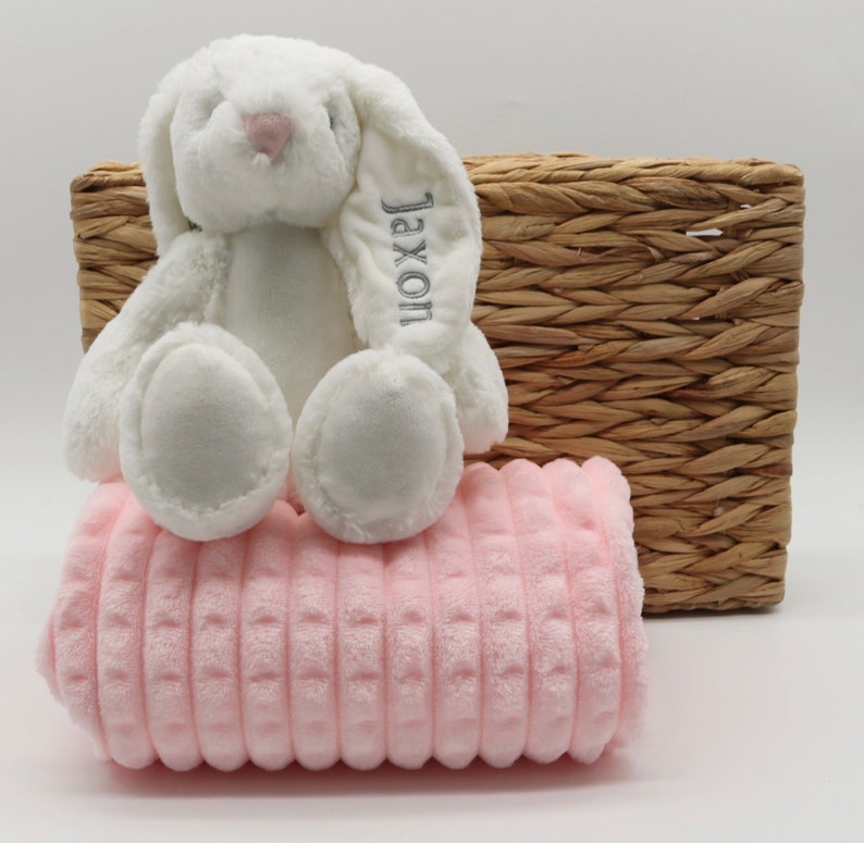 May include: A white plush bunny with a pink nose and the name "Jaxon" embroidered on its ear, sitting on a pink quilted blanket.