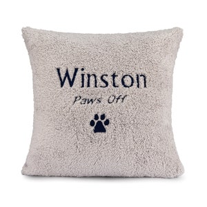 May include: A light gray plush pillow with the name "Winston" and the text "Paws Off" embroidered in dark blue. A dark blue paw print is embroidered below the text.
