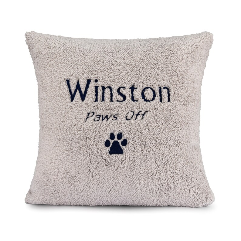 May include: A light gray plush pillow with the name "Winston" and the text "Paws Off" embroidered in dark blue. A dark blue paw print is embroidered below the text.