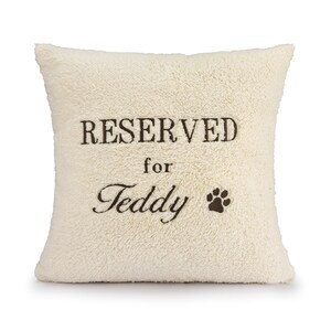 May include: A white plush pillow with the text "RESERVED for Teddy" and a paw print embroidered on it.