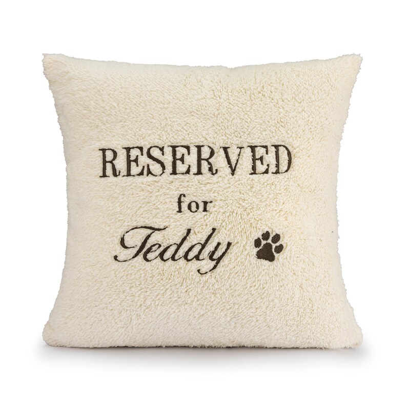 May include: A white plush pillow with the text "RESERVED for Teddy" and a paw print embroidered on it.