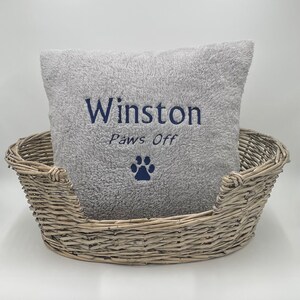 May include: A gray plush dog bed with a gray pillow that says "Winston Paws Off" with a paw print in navy blue.