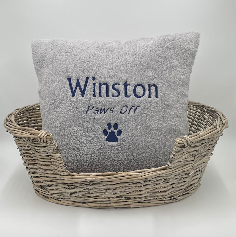 May include: A gray plush dog bed with a gray pillow that says "Winston Paws Off" with a paw print in navy blue.