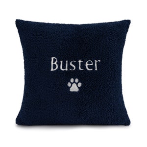May include: A navy blue plush pillow with the name "Buster" embroidered in white with a white paw print below it.